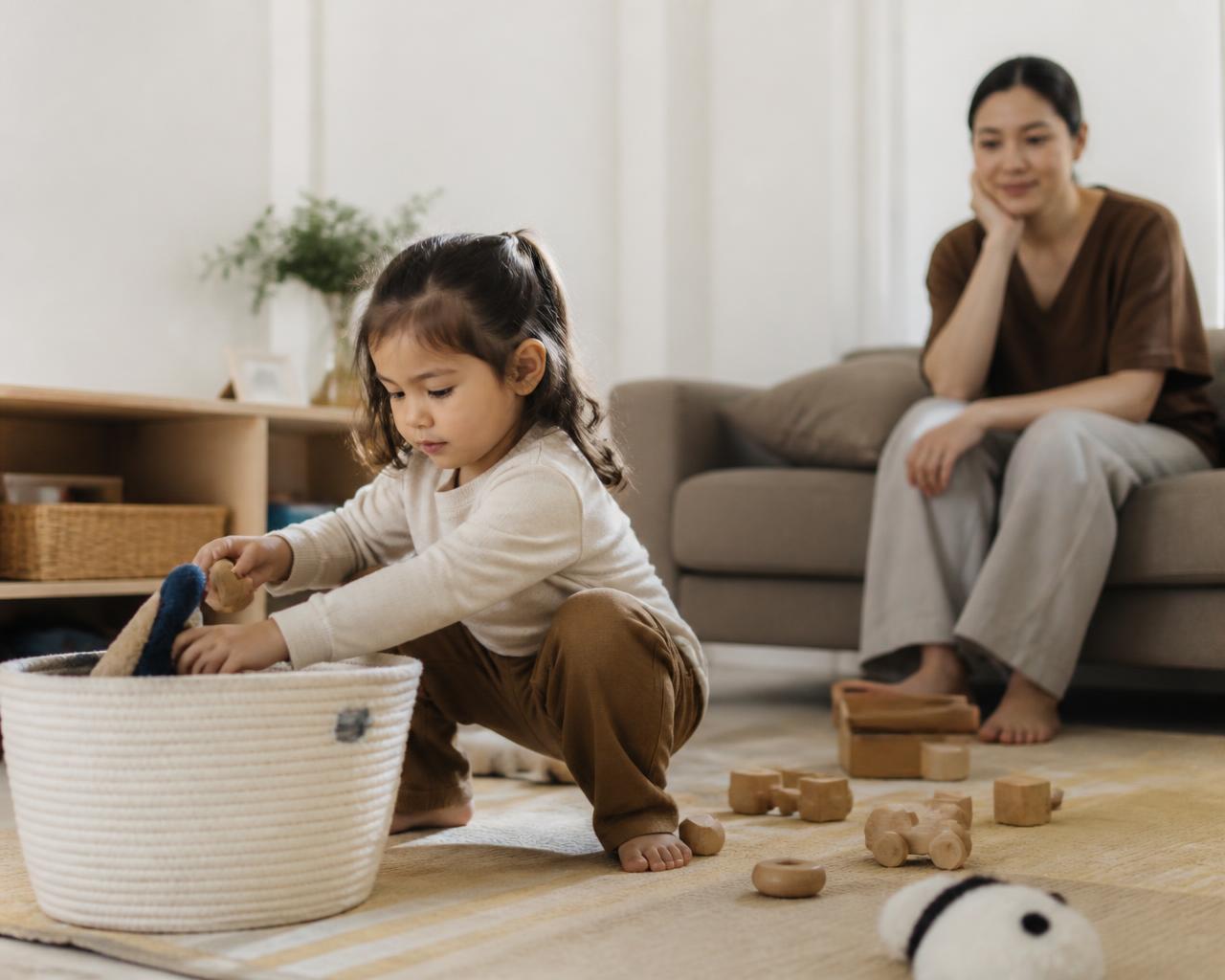 Criança guardando brinquedos sozinha enquanto a mãe observa com calma